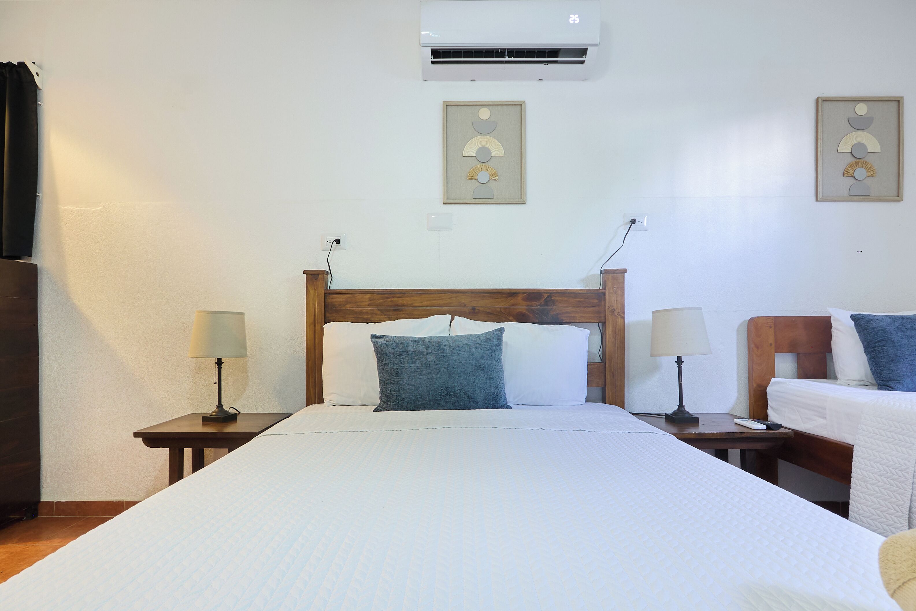 A hotel room with a large bed, two bedside tables with lamps, a wooden headboard, and wall-mounted air conditioning.