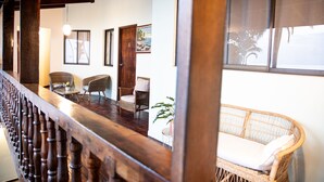 A wooden staircase with a balustrade leading to a room with wicker furniture, a window with a view, and a door with a number. - Hotel Perla de la Playa (Tamarindo)