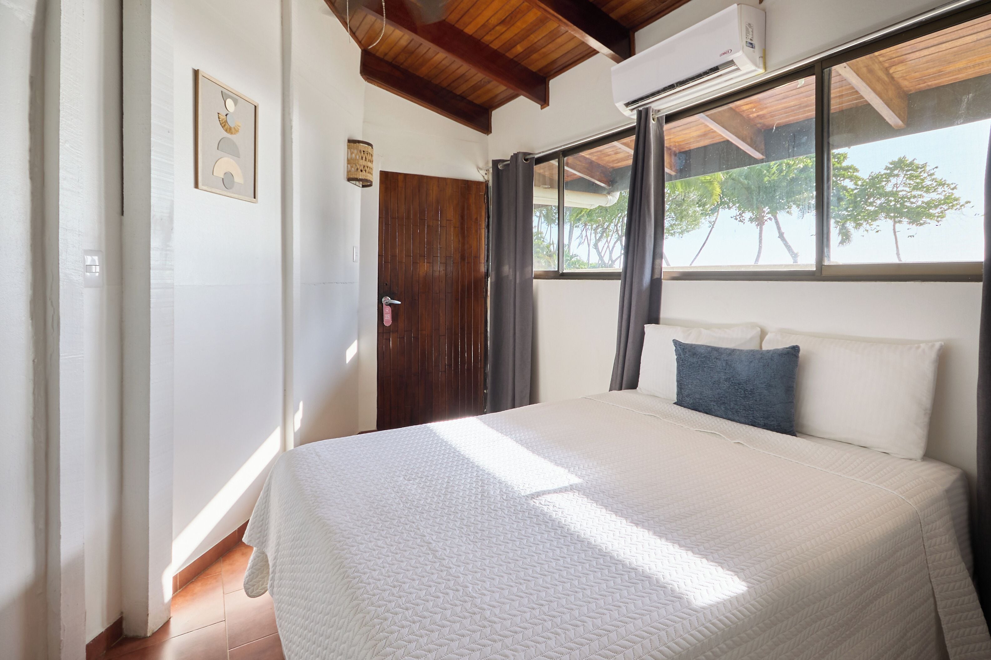 A bedroom with a bed, a window, a door, and an air conditioning unit.