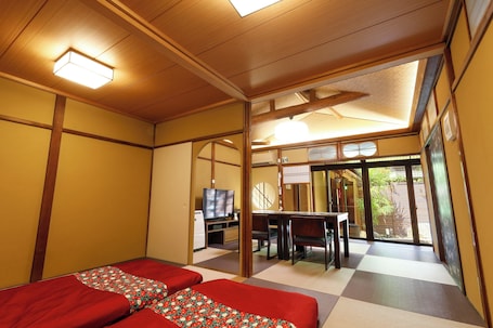 A traditional Japanese-style room with tatami flooring, a low table with chairs, and a television.