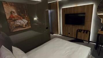 Et moderne hotelværelse med en stor seng, et fladskærms-tv monteret på væggen og et billede over sengen.