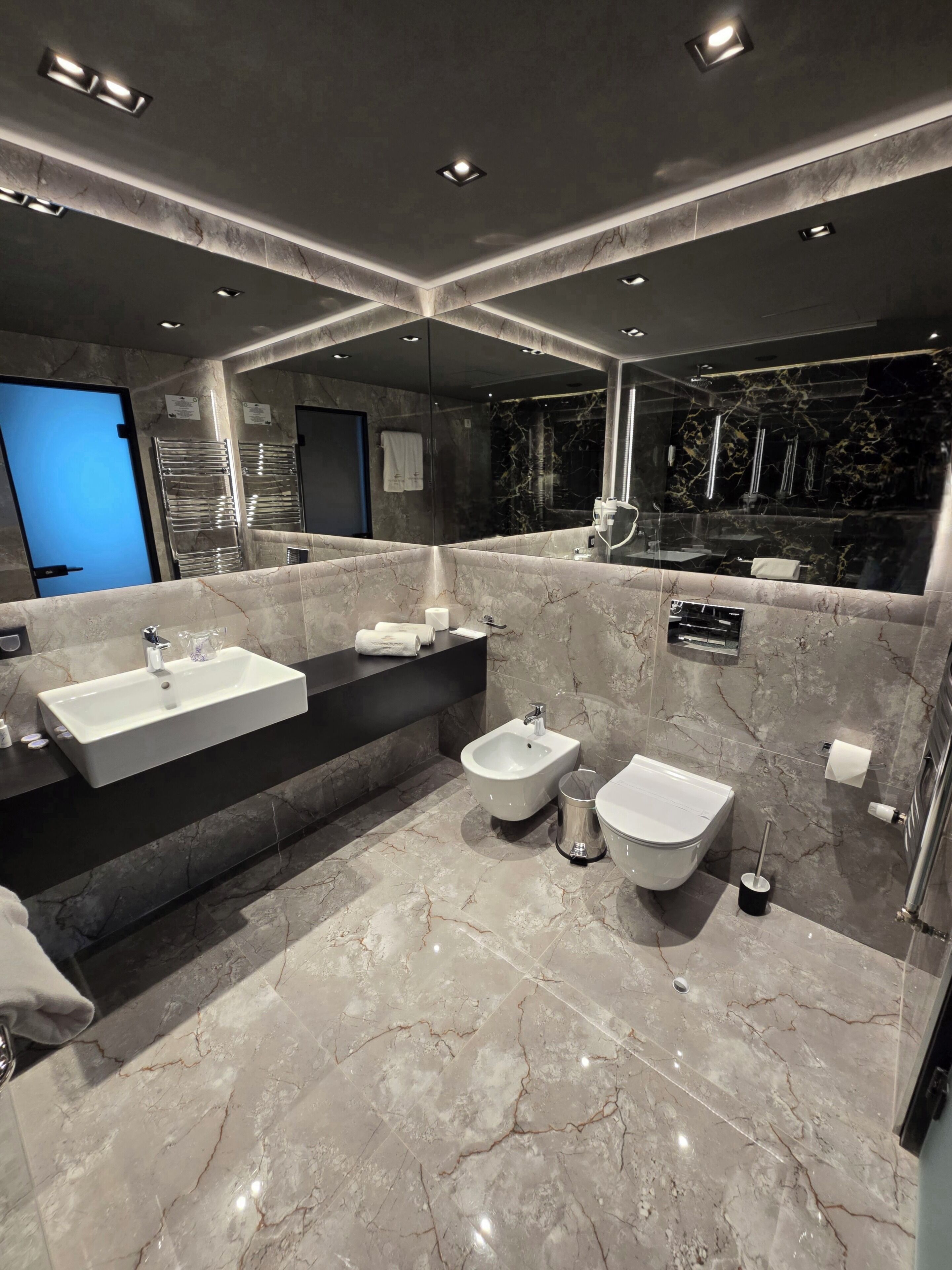 A modern bathroom with a large mirror, two sinks, a bidet, and a bathtub.