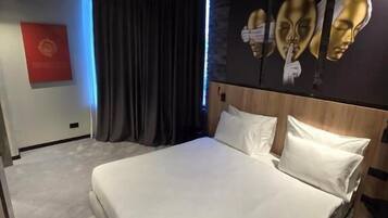 Una habitación de hotel moderna con una cama grande, cortinas oscuras, una cámara de seguridad montada en el techo y una pared con tres máscaras doradas.