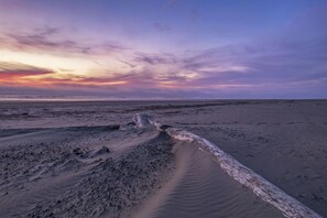 Een strandscène met een houten boomstam op de voorgrond en een rustige zee onder een kleurrijke zonsondergang.