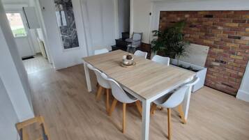 Un comedor con una mesa de madera y sillas blancas, una chimenea de ladrillo y vistas a la cocina.