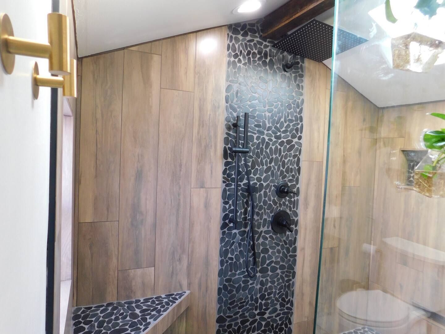 A modern bathroom with a wooden floor, a stone wall, and a glass shower enclosure.