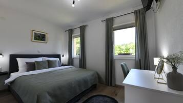 A bedroom with a bed, bedside table, lamp, curtains, and a desk with a vase and mirror.