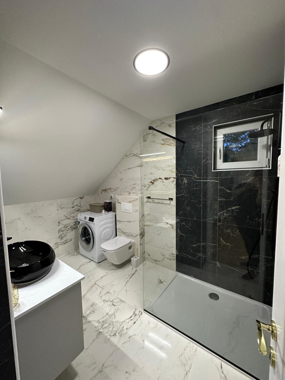 Une salle de bain moderne avec une douche à parois de verre, un lave-linge encastré et des toilettes.