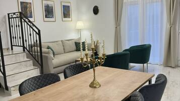 Ett modernt vardagsrum med ett matbord, stolar, en kristallkrona, en trappa och en soffa.