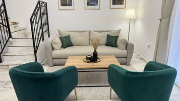 Una sala de estar con un sofá color beige, dos sillones turquesa, una mesa de centro y una escalera con barandillas negras.