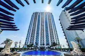 A tall hotel with a swimming pool in the foreground, surrounded by modern architecture and stone sculptures. - Trillium Apartment - Cozy and Bright Downtown Surabaya by Le Ciel Hospitality (Jawa Timur)