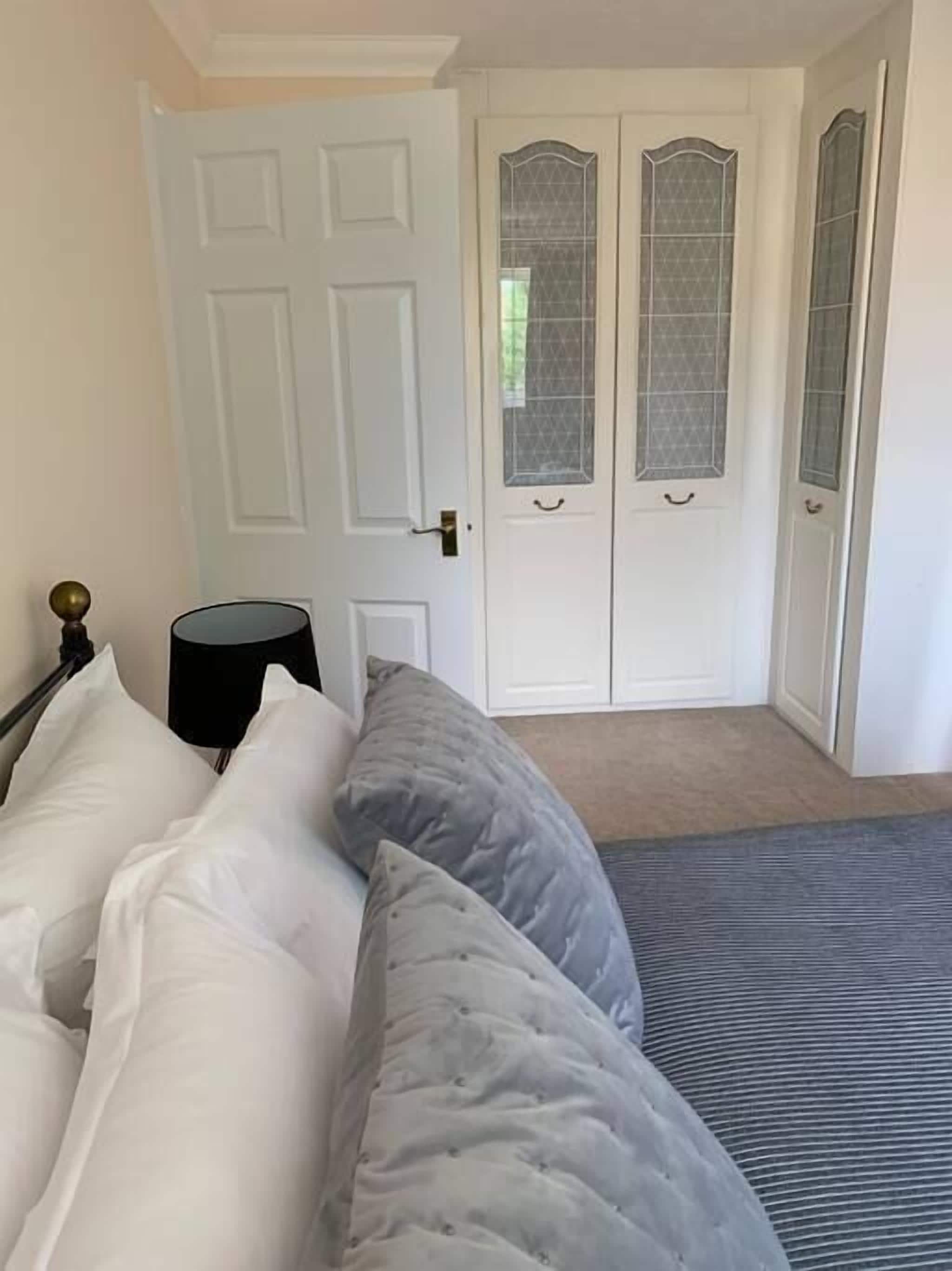 Een slaapkamer met een bed, kussens, een nachtkastje en een deur met ruitpanelen.