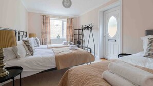 A hotel room with two beds, a window with curtains, a door with an oval glass panel, and a hanging coat rack. - Thorn House a beautiful large house in Witney (Witney)