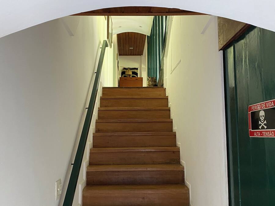 A wooden staircase leading to a room with a green door, a sign indicating a high ceiling, and a cat sitting on the stairs.