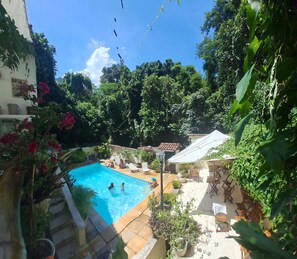 Uma piscina cercada por vegetação exuberante, com algumas pessoas aproveitando a água.