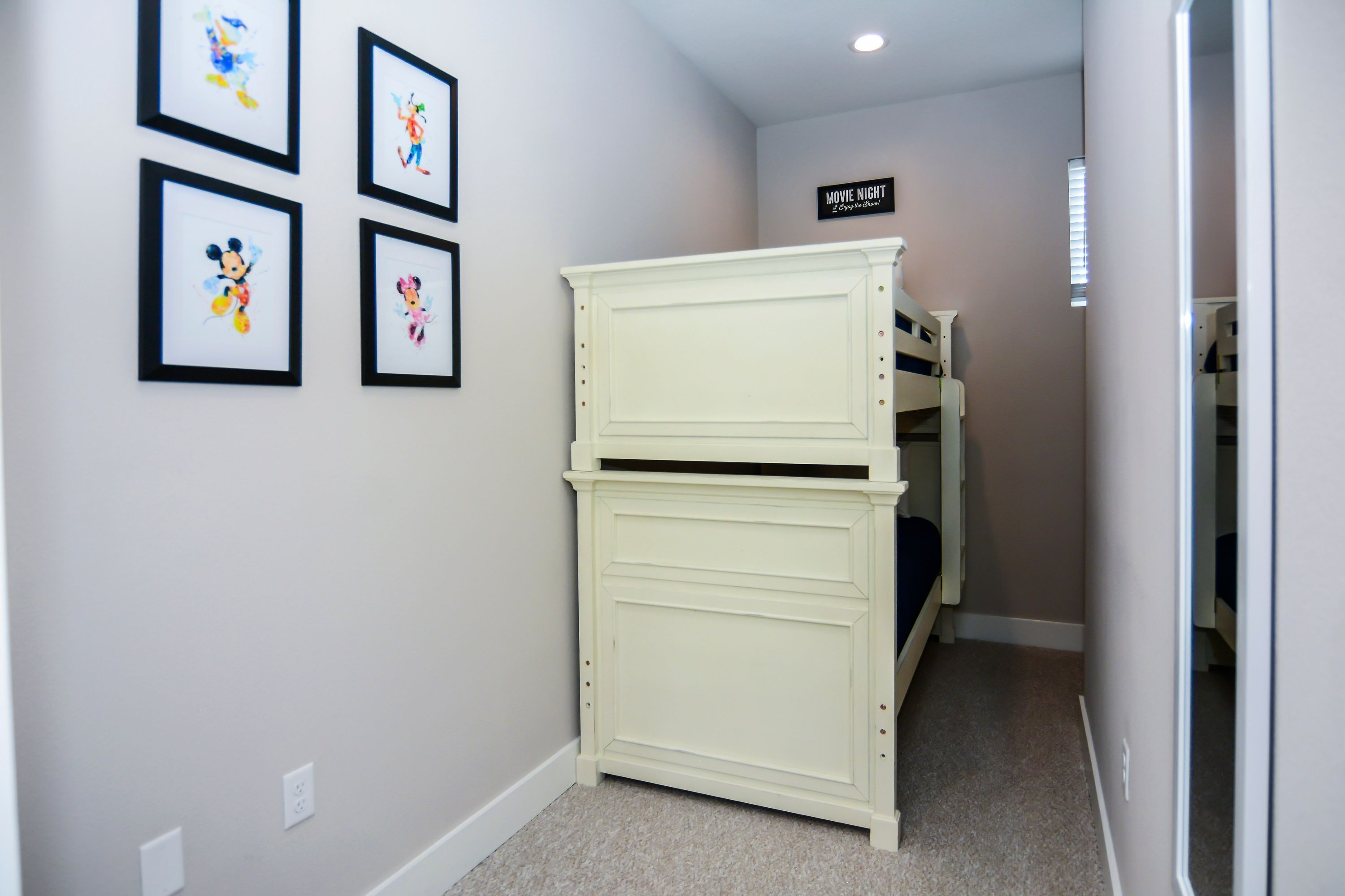 A narrow hallway with a bunk bed and a dresser against the wall. There are framed pictures on the wall and a sign that reads "MOVIE NIGHT".