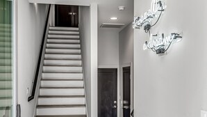 Un intérieur moderne avec un escalier, un panneau lumineux au néon et un canapé beige.