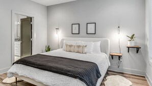 Une chambre à coucher moderne avec un lit, des tables de chevet, un tapis blanc et une porte.