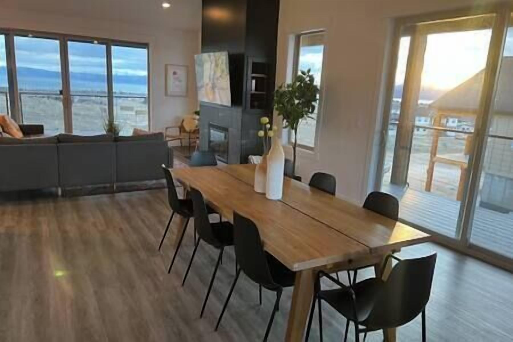A dining area with a wooden table and black chairs, a sofa, and a view of the ocean through large windows.