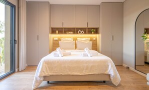 Quarto moderno com cama grande, roupeiro embutido e mesa de cabeceira com abajur.