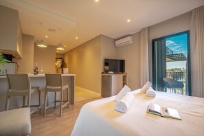 Quarto de hotel com cama, escrivaninha, cadeiras, televisão e varanda com vista.