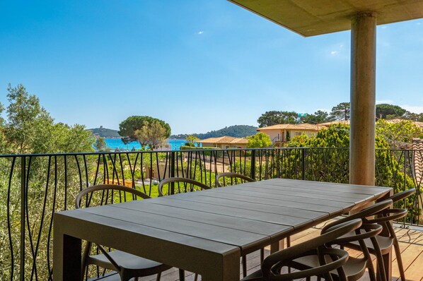 A balcony with a table and chairs, overlooking a scenic view of a hill and a body of water.