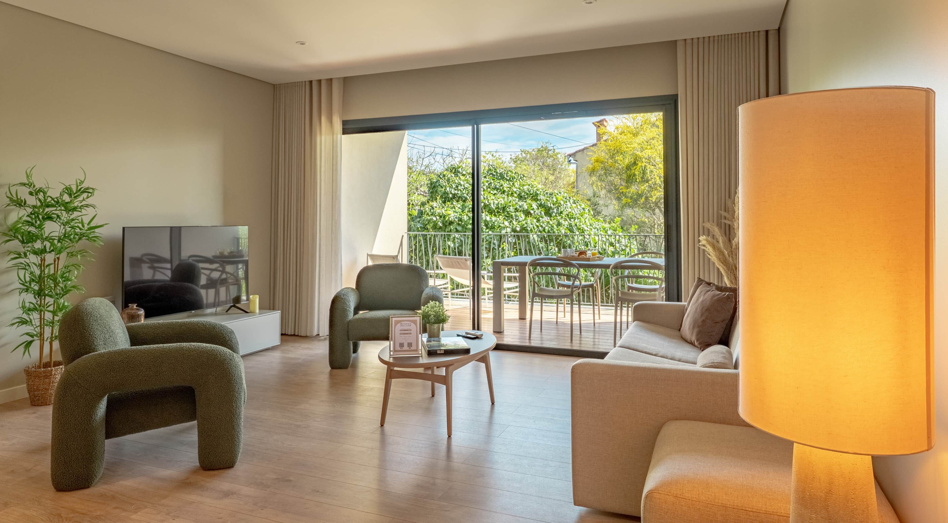 A modern living room with a sofa, armchair, TV, and a balcony with outdoor furniture.
