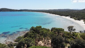 A coastal landscape with a sandy beach, clear turquoise waters, and dense green trees in the foreground.