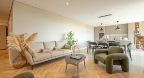A modern living room with a sofa, coffee table, and chairs, a dining area with a table and chairs, and a kitchen in the background. - Apartment no. 301 (Zonza)