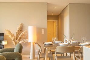 Un coin repas avec une table dressée pour quatre personnes, des chaises, une lampe et un vase contenant des plumes d’herbe de la pampa.