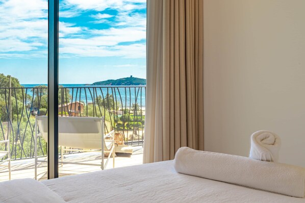 Ein Hotelzimmer mit einem großen Bett, Meerblick, einem Balkon mit einem Stuhl und Vorhängen.