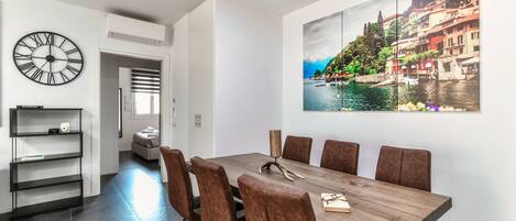 A dining area with a wooden table, brown upholstered chairs, and a large painting of a coastal town.