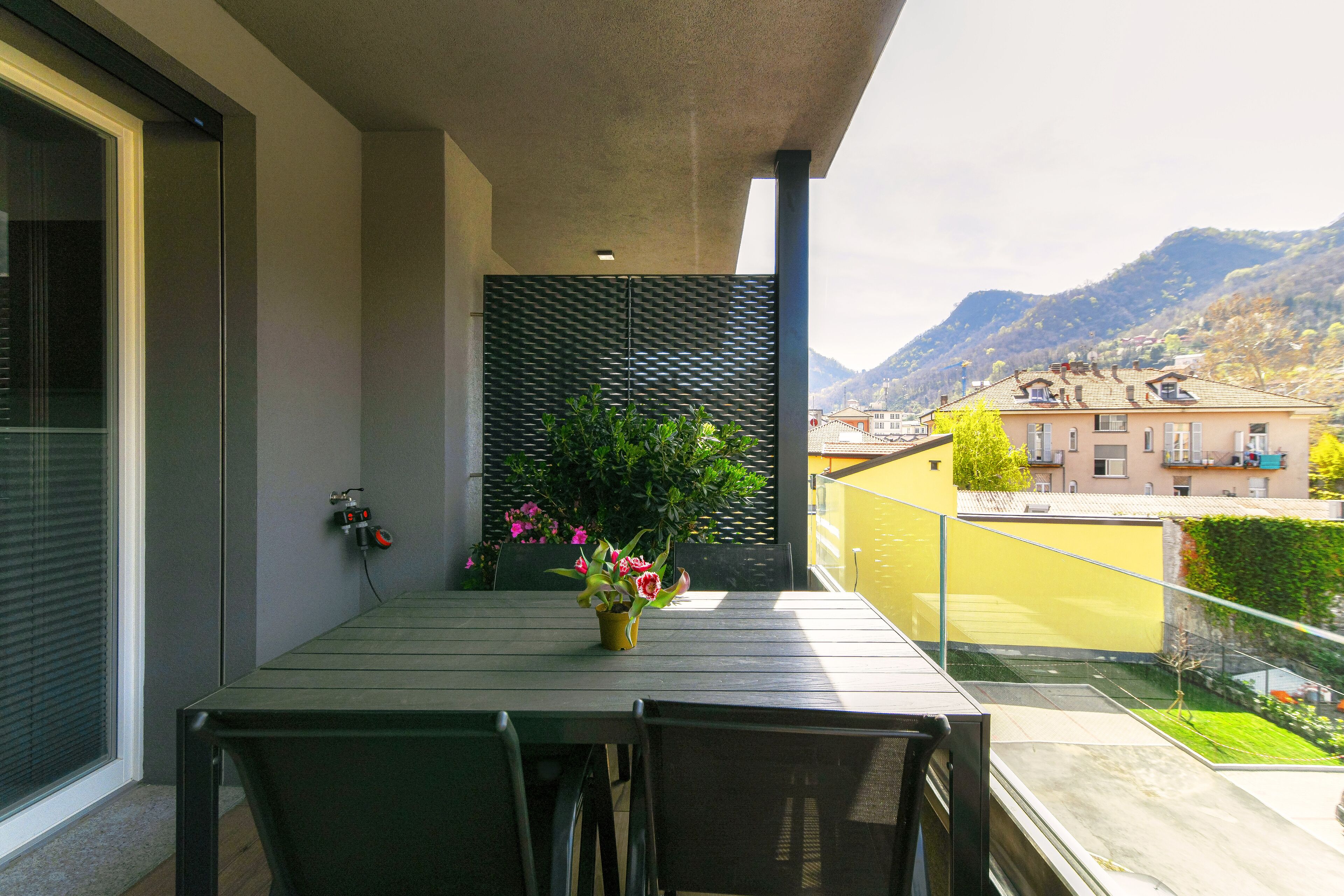 Ein Balkon mit Tisch und Stühlen, einem Blumentopf und Blick auf einen Berg und Gebäude.