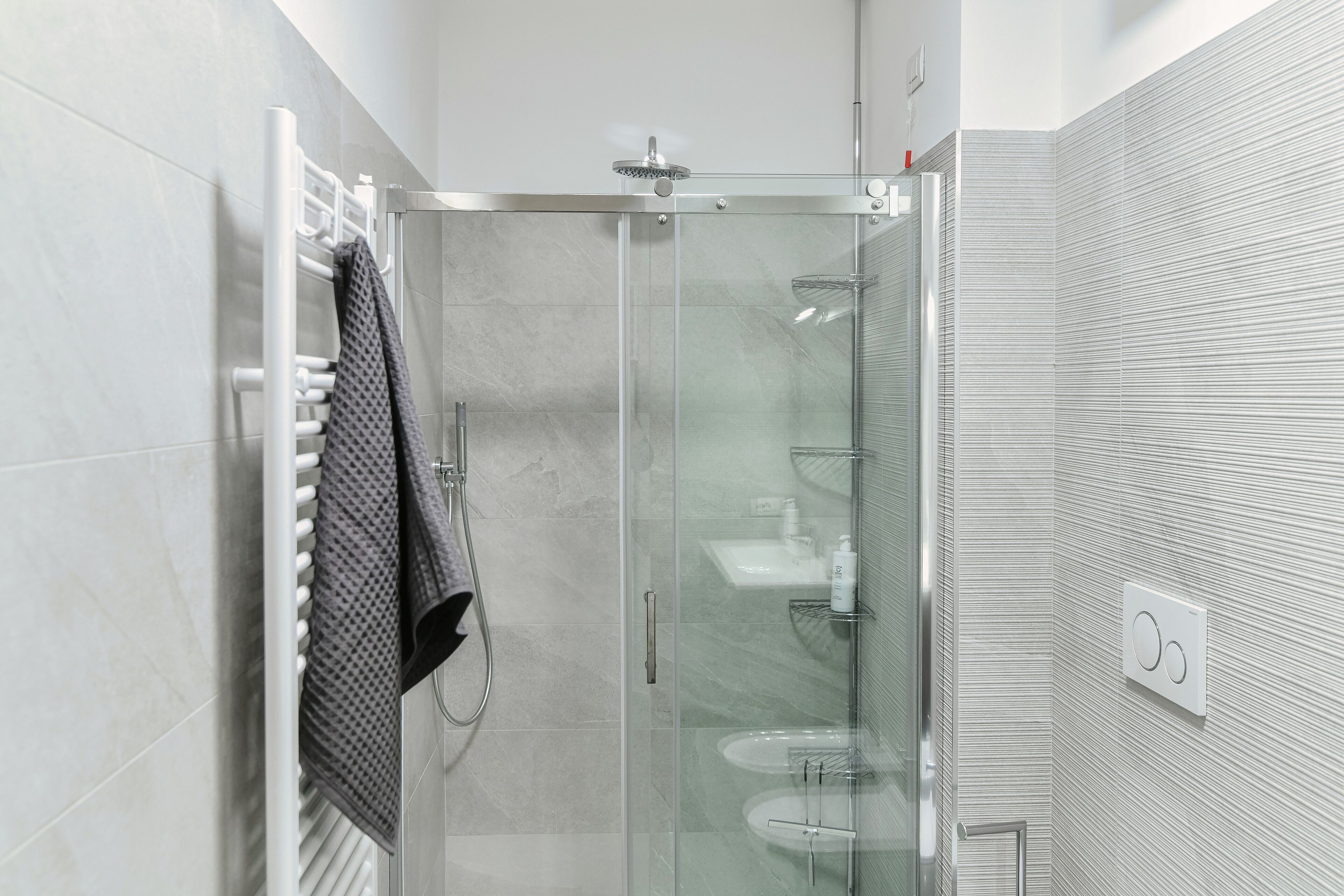 Ein modernes Badezimmer mit einer gläsernen Dusche, einem Handtuchhalter und einer weißen Fliesenwand.