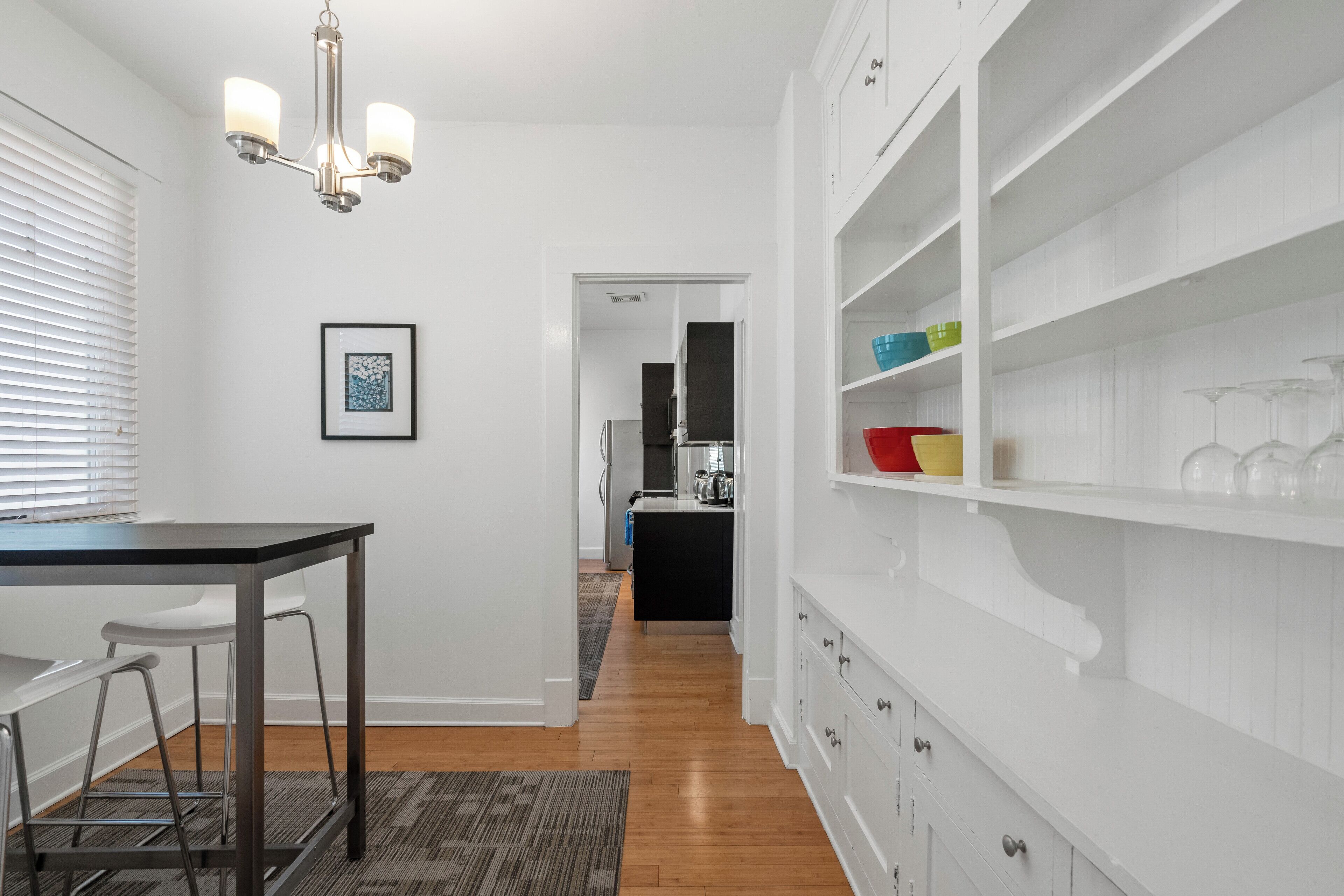 Una cocina moderna con armarios blancos, un comedor con mesa y sillas, y un pasillo que conduce a una zona de cocina.