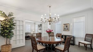 A dining room with a round wooden table, six chairs, a chandelier, a potted plant, and a bookshelf. - Standish House by BCA Furnished Apts (Atlanta)