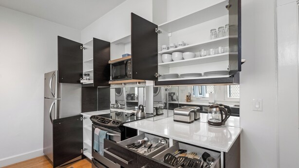 A modern kitchen with a built-in microwave, toaster, and oven. There are open cabinets with dishes and utensils. - Standish House by BCA Furnished Apts (Atlanta)