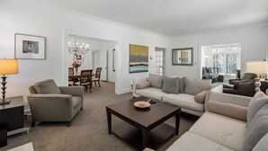A modern living room with a sofa, armchairs, a coffee table, and a dining area with chairs and a chandelier. - Standish House by BCA Furnished Apts (Atlanta)