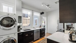 A modern kitchen with a built-in washer and dryer, a large window, and a coffee maker on the counter. - Standish House by BCA Furnished Apts (Atlanta)