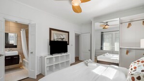 A hotel room with a large bed, a television, a bathroom with a bathtub, and a ceiling fan. - Standish House by BCA Furnished Apts (Atlanta)
