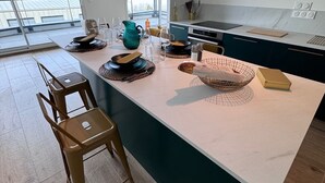 Uma cozinha moderna com uma ilha grande, cadeiras de madeira e vista para o mar.