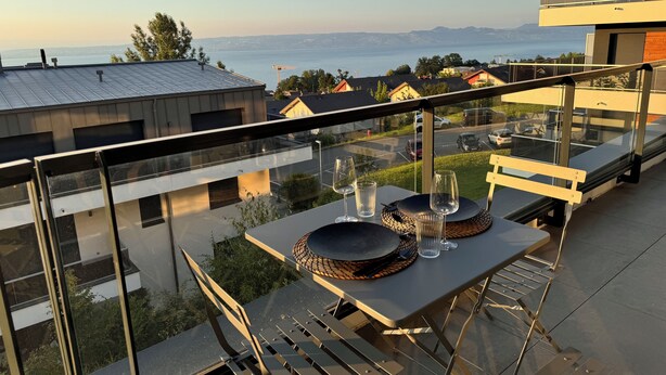Varanda com mesa posta para dois, vista para a cidade e um corpo de água.