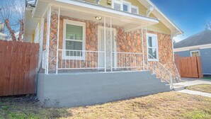 A two-story house with a stone facade, a front porch with white railings, and a wooden fence. - Wonderful 3 BR 2 BA Near Downtown (San Antonio)