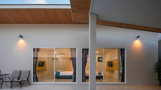 A modern hotel room with a large sliding glass door, a small seating area with chairs, and a visible bed with a blue accent. - Sasi Pool Villa Phuket (Rawai)