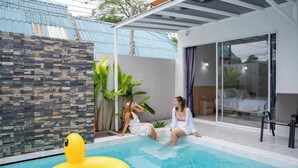 A modern outdoor pool area with a stone wall, a yellow inflatable ring, and a glass door leading to a bedroom. - Sasi Pool Villa Phuket (Rawai)