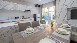 A modern kitchen with marble countertops, a dining area with a marble table, and a TV mounted on the wall. - Sasi Pool Villa Phuket (Rawai)