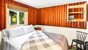 Ein Schlafzimmer mit einem großen Bett, einem Fenster mit Blick auf Grünflächen, einer Holzablage mit Büchern und einem Sessel.