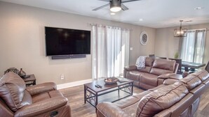 A modern living room with leather sofas, a flat-screen TV, and a ceiling fan. - Lovely 3 BR Home Only 9 Minutes From Downtown (San Antonio)