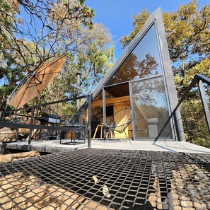 Une cabane moderne aux murs de verre et à la structure métallique, entourée d’arbres.