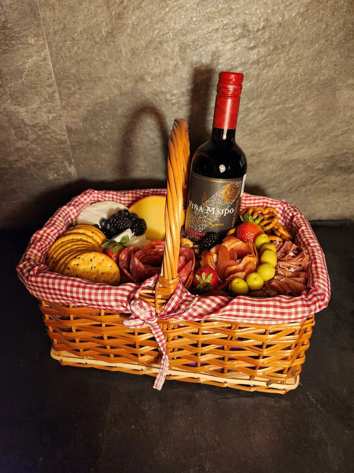A wicker basket filled with various food items and a bottle of Vina Maipo wine.